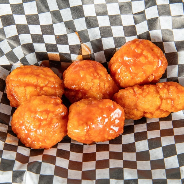 Six orange, saucy boneless wings in a black and white checkered paper-lined basket.