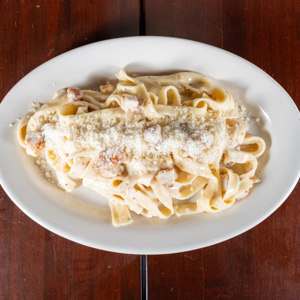 Creamy fettuccine alfredo with chicken and grated Parmesan cheese on a white oval plate.