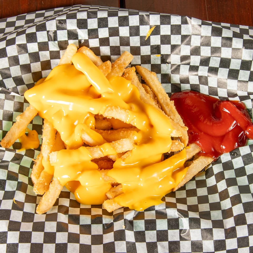 Cheesy fries with a side of ketchup in a black and white checkered paper tray.