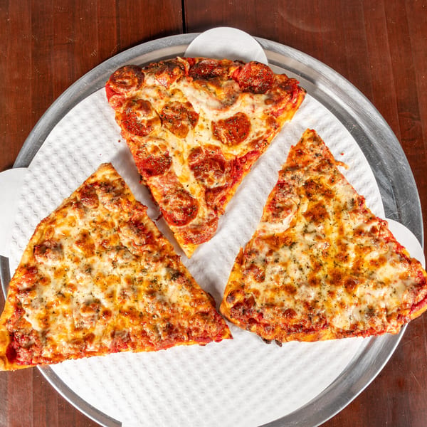 Three slices of pizza, one pepperoni and two sausage, on a metal tray with a white liner.