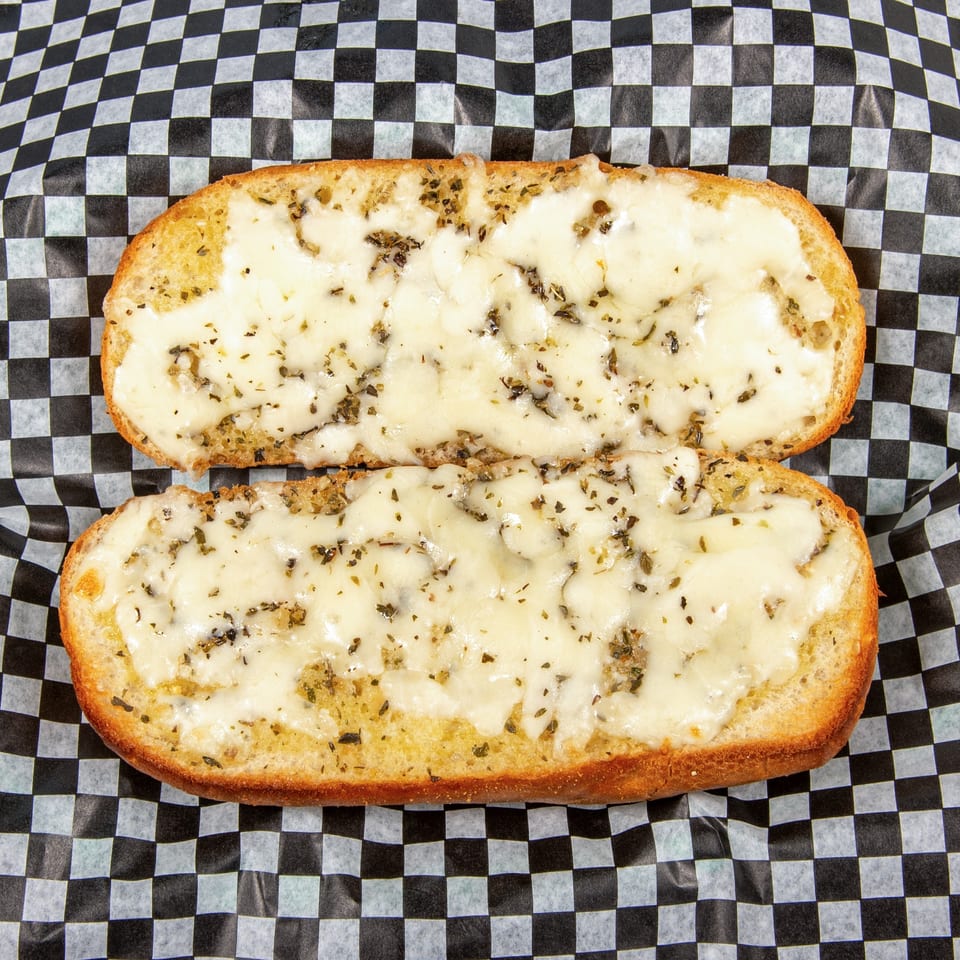 Two halves of cheesy garlic bread with herbs on black and white checkered paper.