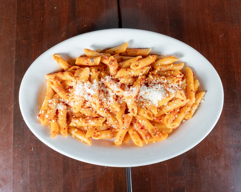 Penne pasta in a creamy red sauce, topped with grated cheese and red pepper flakes.