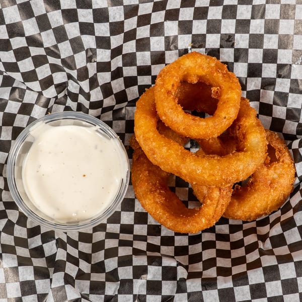 Golden-brown onion rings and a side of creamy dipping sauce on black and white checkered paper.