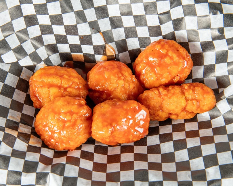 Six orange, saucy boneless wings in a black and white checkered paper basket.