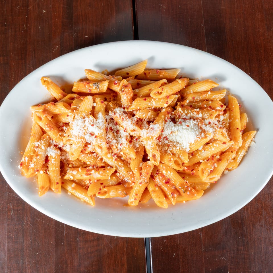 Penne pasta with red sauce, parmesan cheese, and red pepper flakes on a white plate.